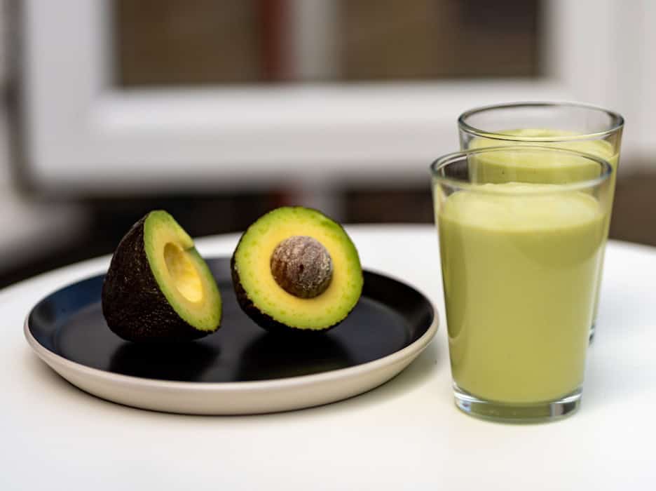 an avocado on a plate next to a glass of juice